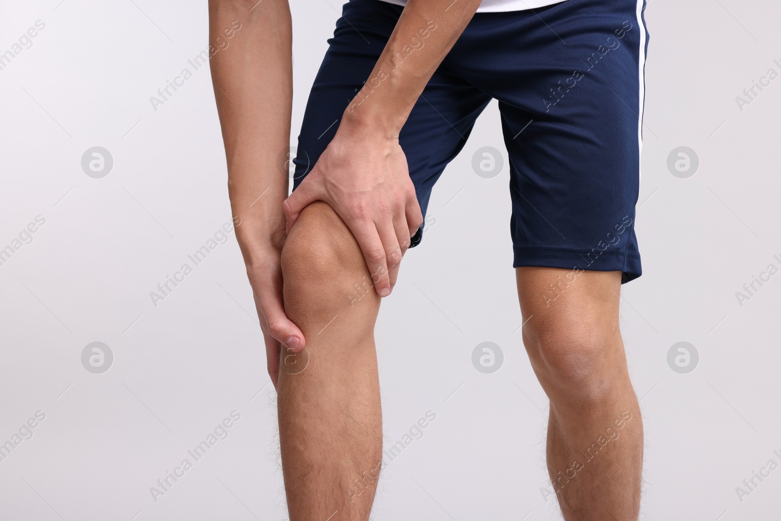 Photo of Young man suffering from pain in knee on light grey background, closeup