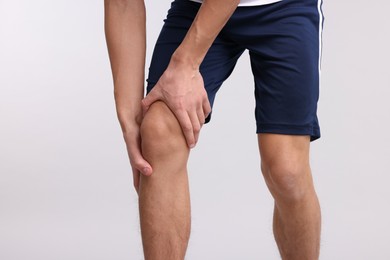 Photo of Young man suffering from pain in knee on light grey background, closeup