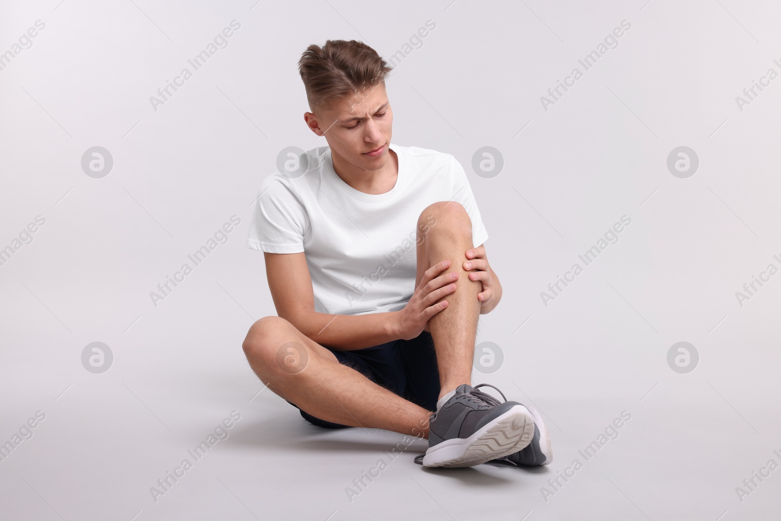 Photo of Young man suffering from pain in knee on light grey background