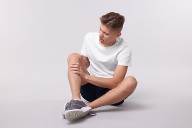 Photo of Young man suffering from pain in knee on light grey background