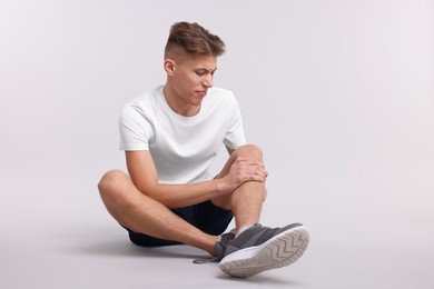 Young man suffering from pain in knee on light grey background