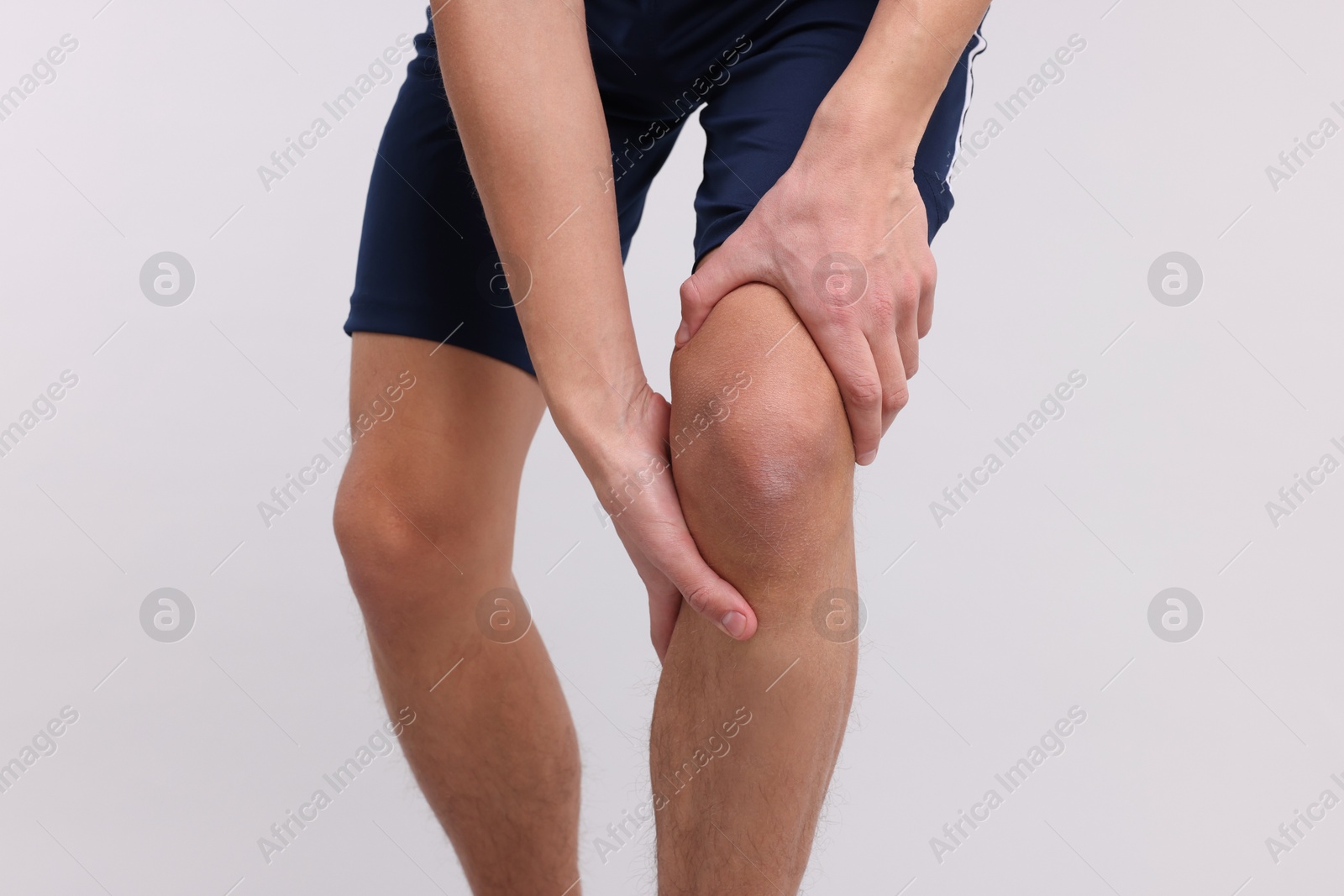 Photo of Young man suffering from pain in knee on light grey background, closeup