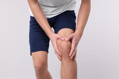 Photo of Young man suffering from pain in knee on light grey background, closeup