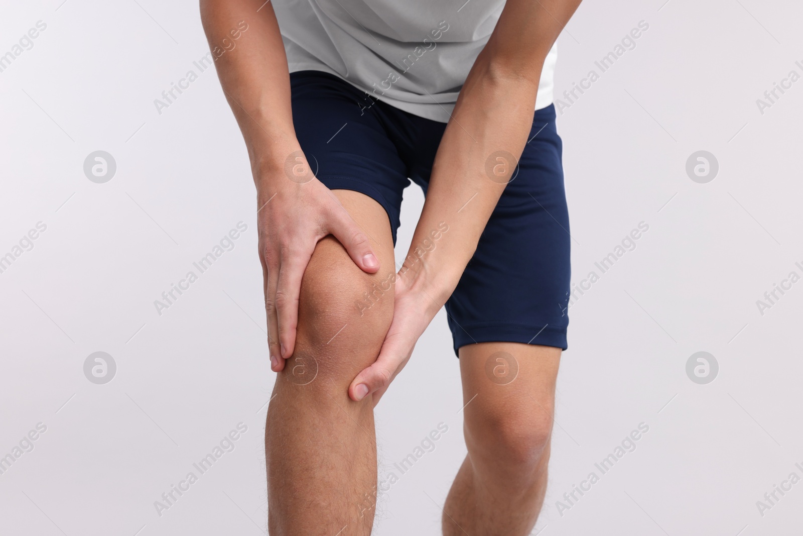 Photo of Young man suffering from pain in knee on light grey background, closeup