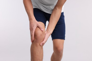 Photo of Young man suffering from pain in knee on light grey background, closeup