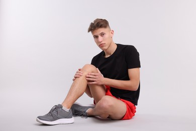 Young man suffering from pain in knee on light grey background