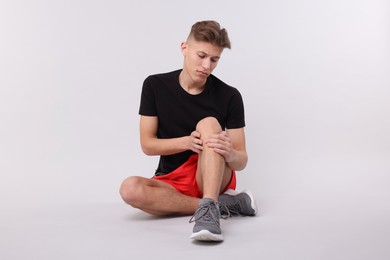 Photo of Young man suffering from pain in knee on light grey background