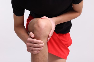 Young man suffering from pain in knee on light grey background, closeup