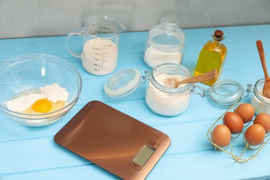 Photo of Electronic kitchen scale and different food products on light blue wooden table indoors, closeup