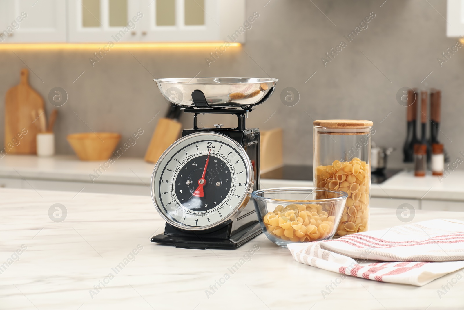 Photo of Retro mechanical kitchen scale and raw pasta on white marble table indoors