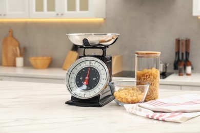 Photo of Retro mechanical kitchen scale and raw pasta on white marble table indoors