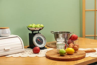 Kitchen scale, products and cooking utensils on wooden table