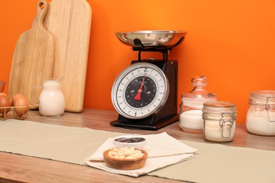 Kitchen scale, products and cooking utensils on wooden table