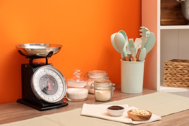 Photo of Kitchen scale, products and cooking utensils on wooden table