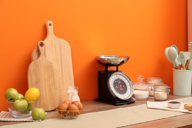 Kitchen scale, products and cooking utensils on wooden table