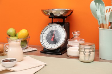 Photo of Kitchen scale, products and cooking utensils on wooden table