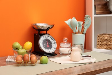 Photo of Kitchen scale, products and cooking utensils on wooden table