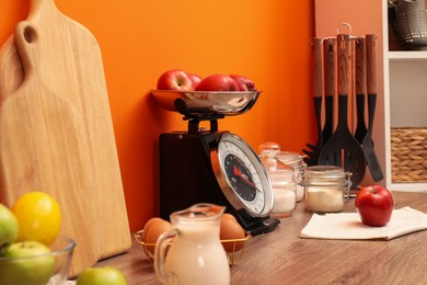 Photo of Kitchen scale, products and cooking utensils on wooden table