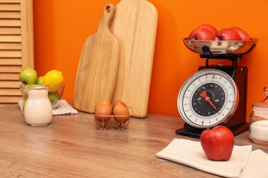 Kitchen scale, products and cooking utensils on wooden table