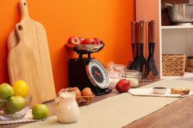 Photo of Kitchen scale, products and cooking utensils on wooden table