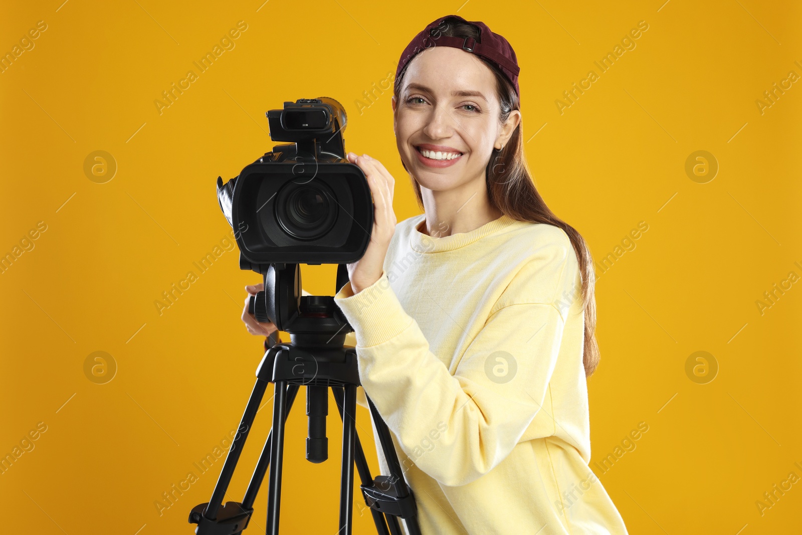 Photo of Happy woman with professional video camera on orange background