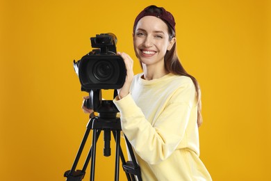 Photo of Happy woman with professional video camera on orange background