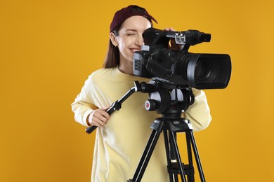 Photo of Happy woman with professional video camera on orange background