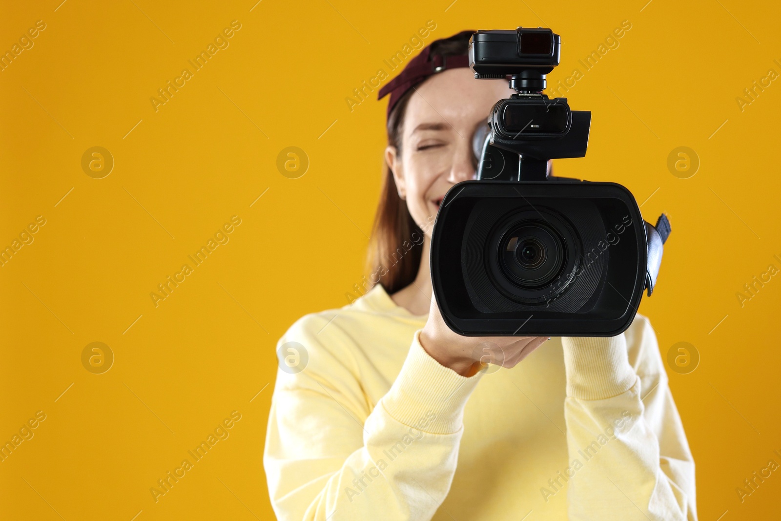 Photo of Happy woman with professional video camera on orange background, selective focus. Space for text