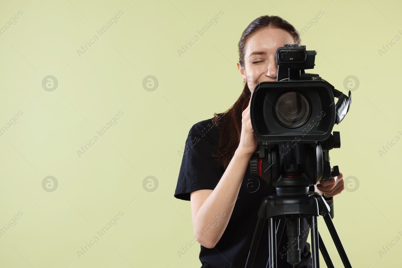 Photo of Woman with professional video camera on pale olive background, space for text