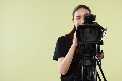 Woman with professional video camera on pale olive background, space for text