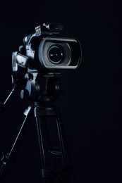 Photo of Modern video camera with tripod on black background