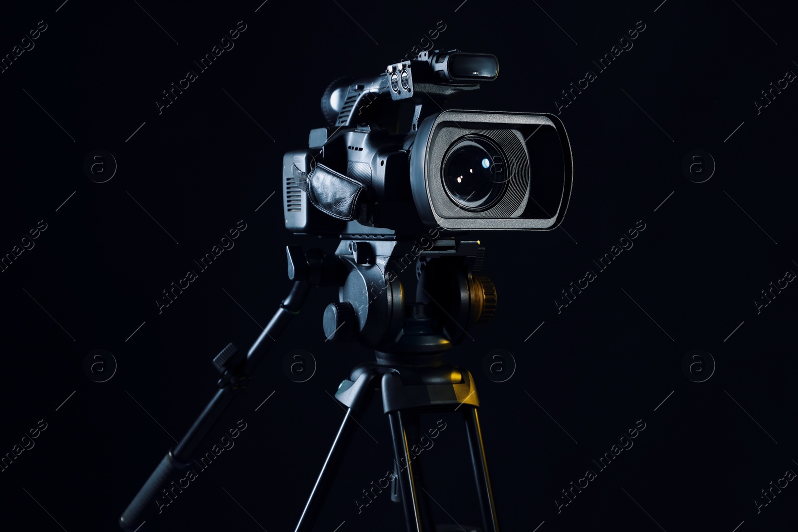 Photo of Modern video camera with tripod on black background