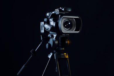 Photo of Modern video camera with tripod on black background