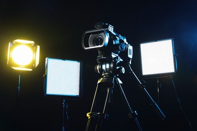 Photo of Modern video camera with tripod and lighting equipment on black background