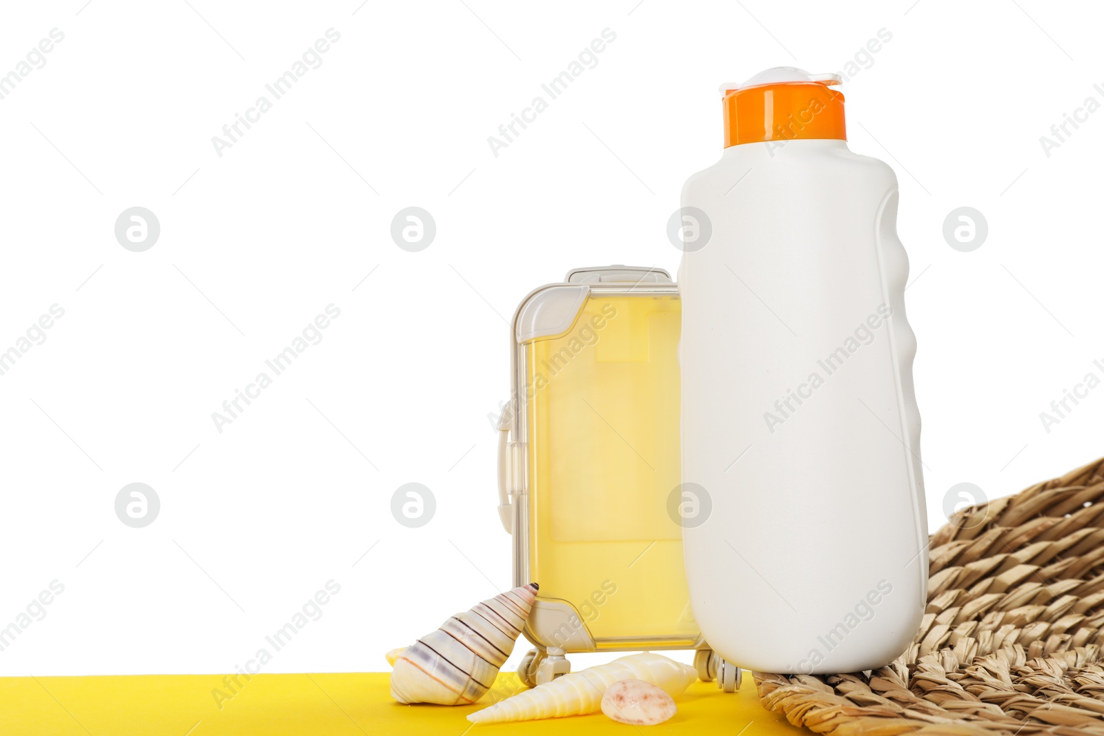 Photo of Bottle of sun protection product and seashells on yellow surface against white background