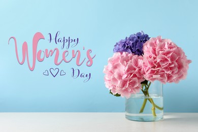 Happy Women's day card. Glass vase with beautiful hydrangea flowers on table against light blue background