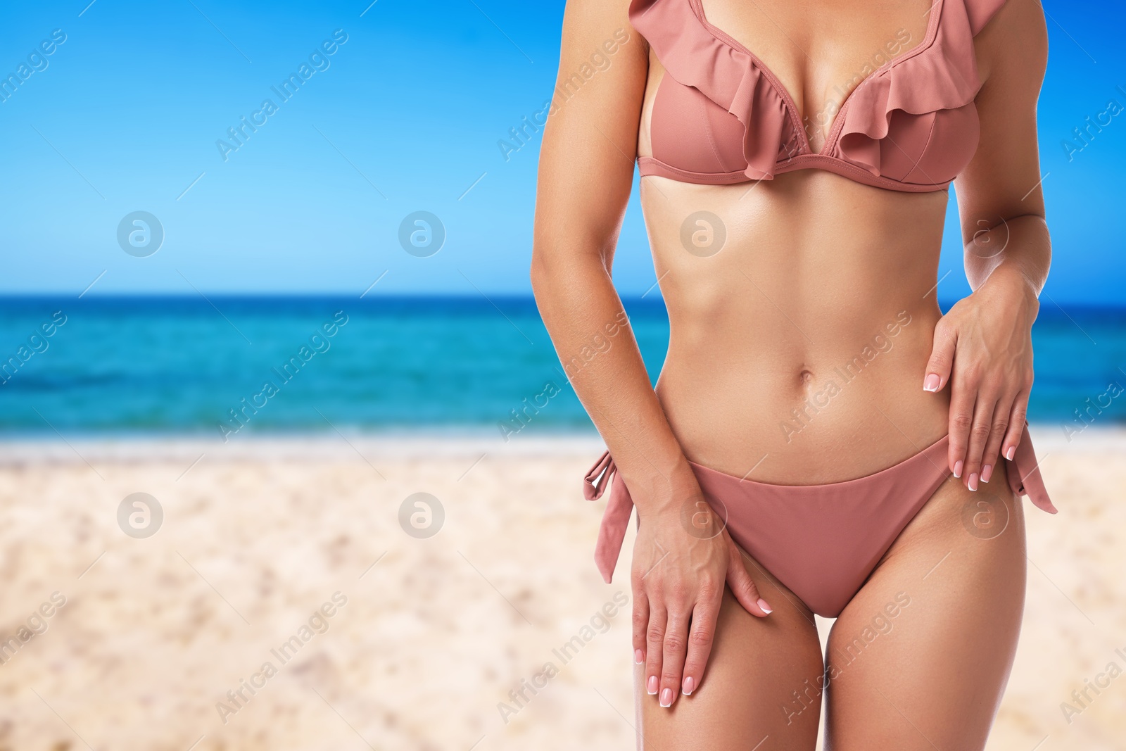 Image of Sexy young woman in pink swimsuit on sandy beach near blue sea, closeup. Space for text