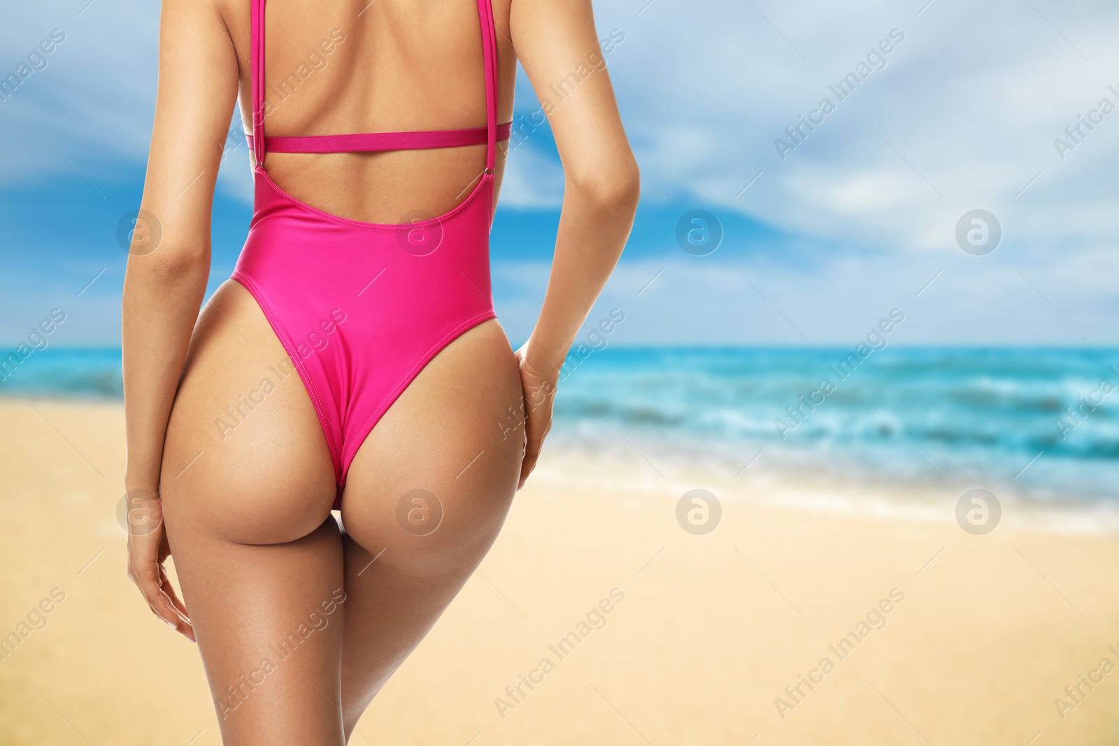 Image of Sexy young woman in pink swimsuit on sandy beach near turquoise sea, closeup. Back view. Space for text