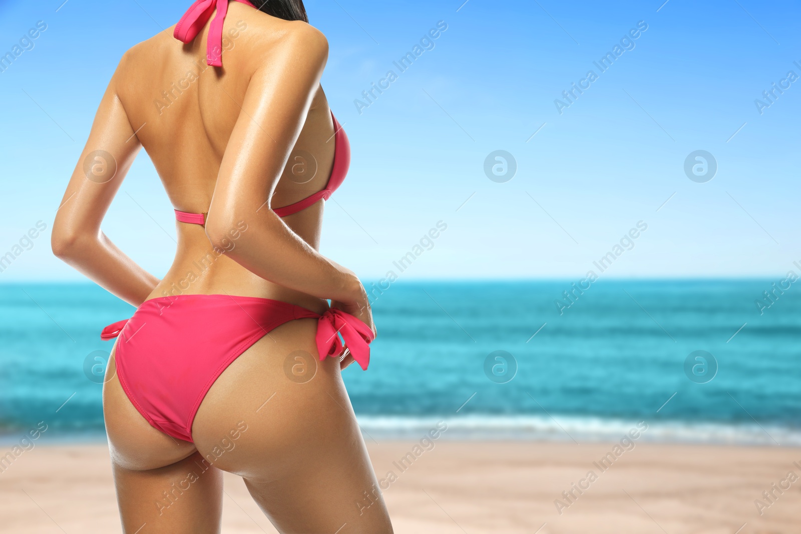 Image of Sexy young woman in pink swimsuit on sandy beach near turquoise sea, closeup. Space for text