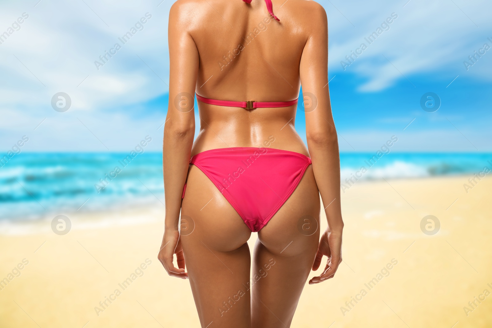 Image of Sexy young woman in pink swimsuit on sandy beach near turquoise sea, closeup. Girl has perfect tanned body, back view