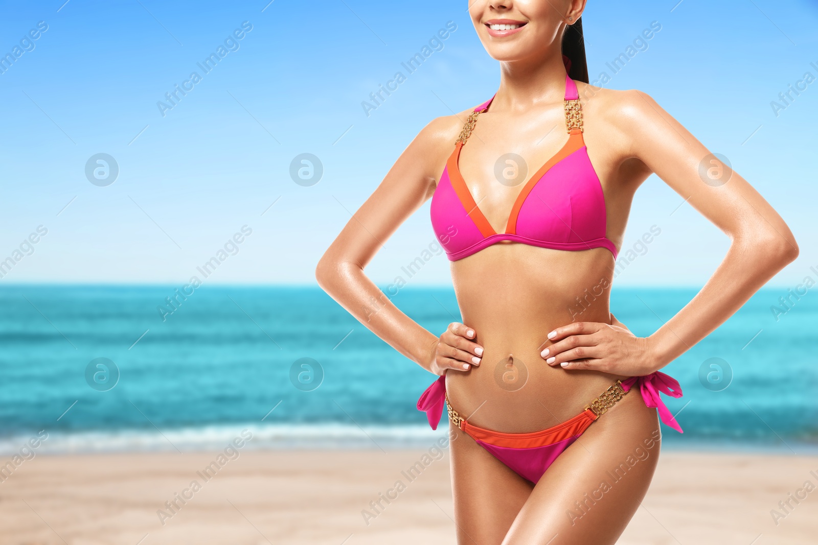 Image of Sexy young woman in pink swimsuit on sandy beach near blue sea, closeup. Space for text