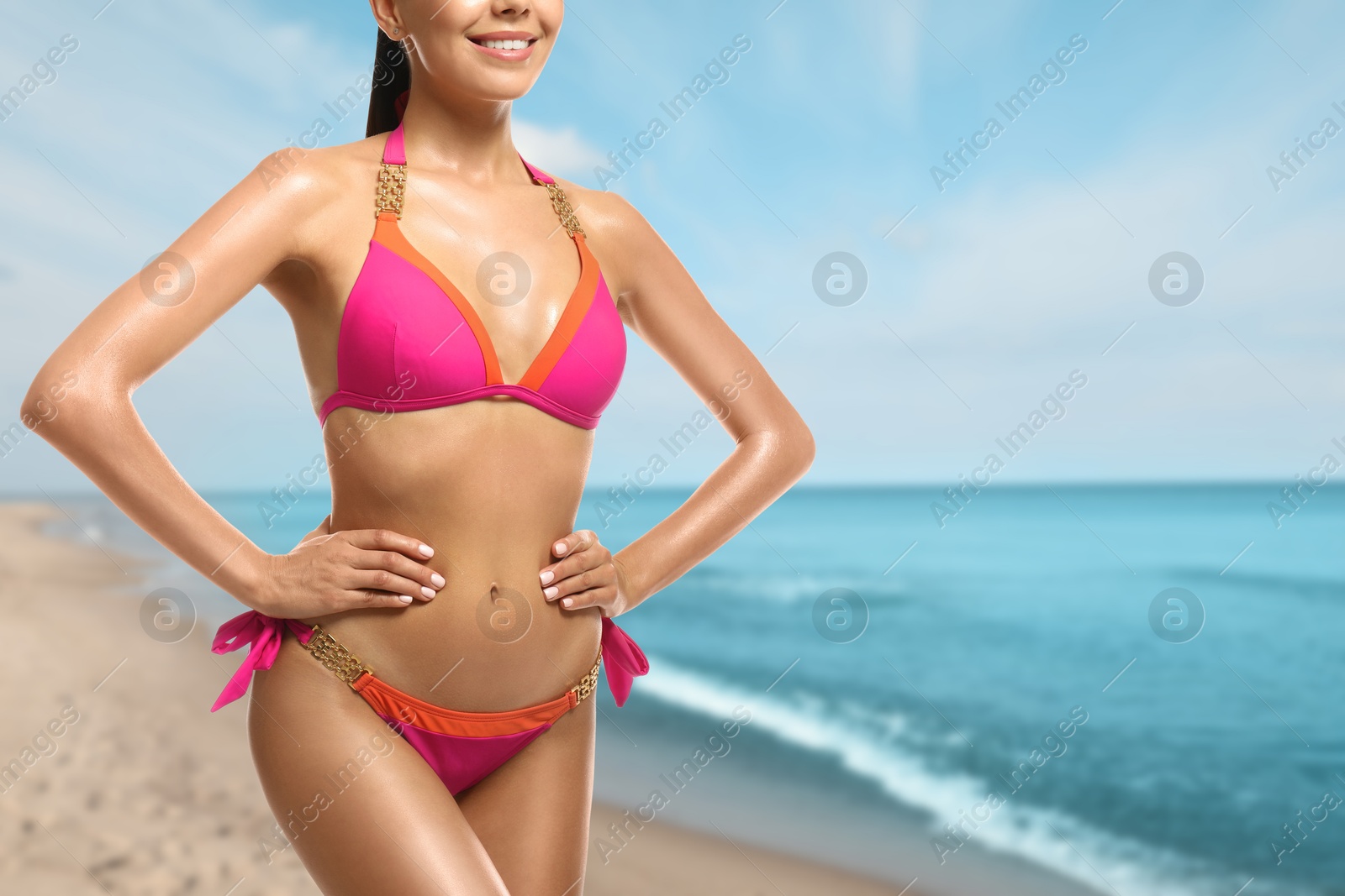 Image of Sexy young woman in pink swimsuit on sandy beach near blue sea, closeup. Space for text