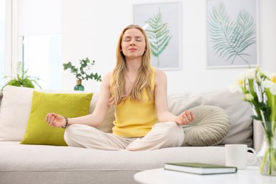 Photo of Feng shui. Young woman meditating on couch at home