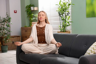 Feng shui. Young woman meditating on couch at home''