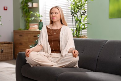 Feng shui. Young woman meditating on couch at home''