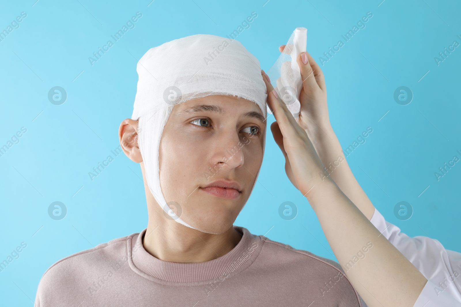 Photo of Doctor bandaging patient's head on light blue background, closeup