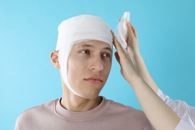 Doctor bandaging patient's head on light blue background, closeup