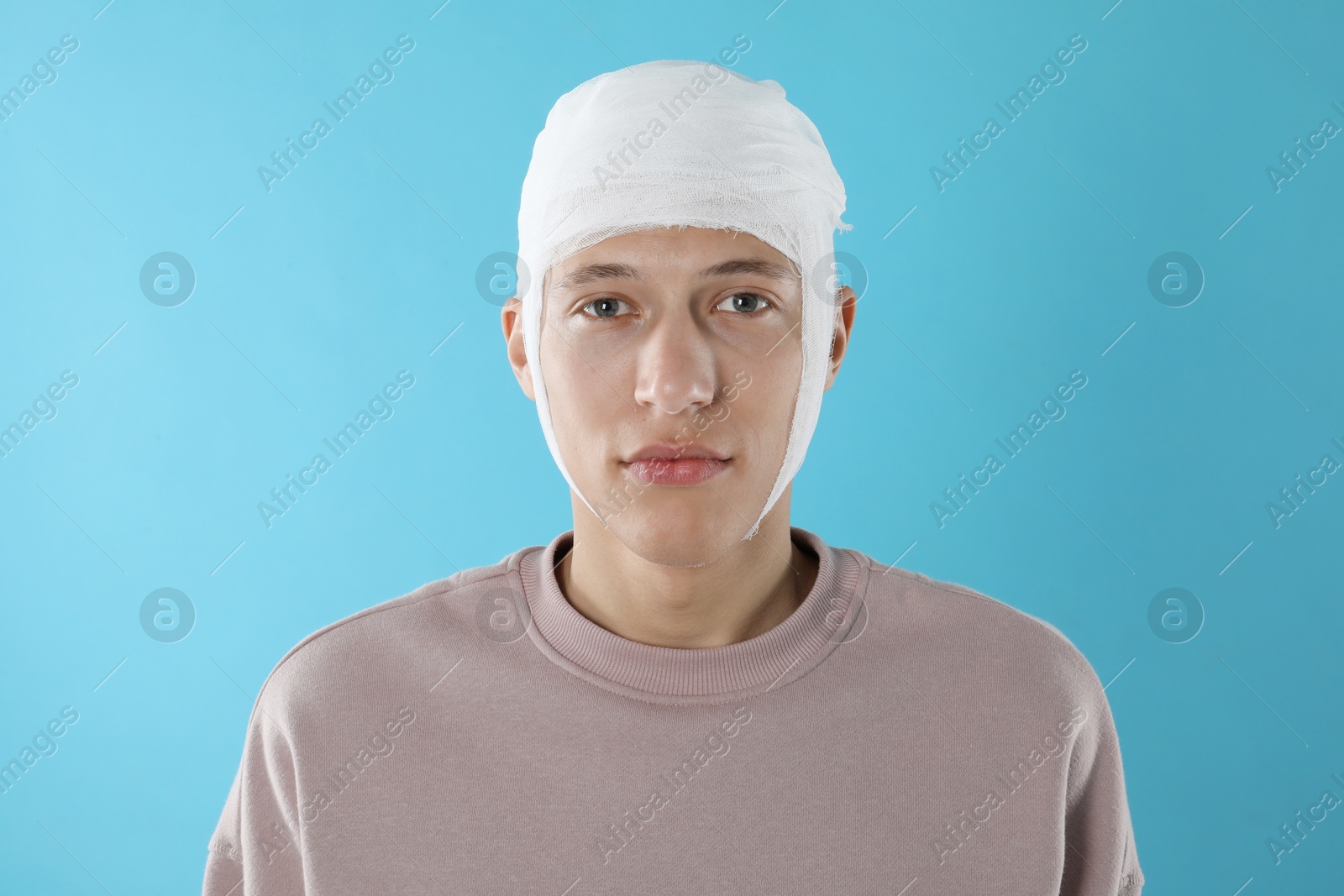 Photo of Man with head wrapped in medical bandage on light blue background