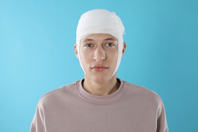 Man with head wrapped in medical bandage on light blue background