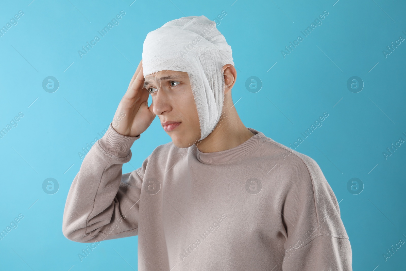 Photo of Man with head wrapped in medical bandage on light blue background